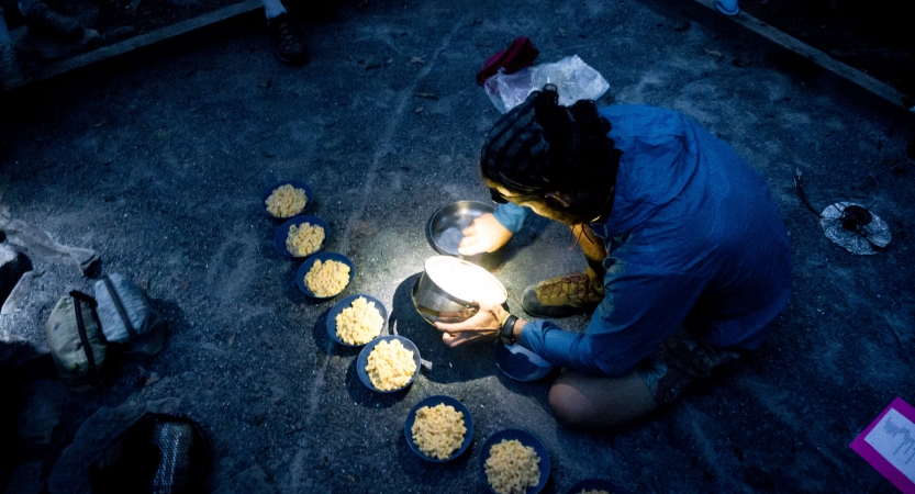 A person prepares bowls of food by headlamp 